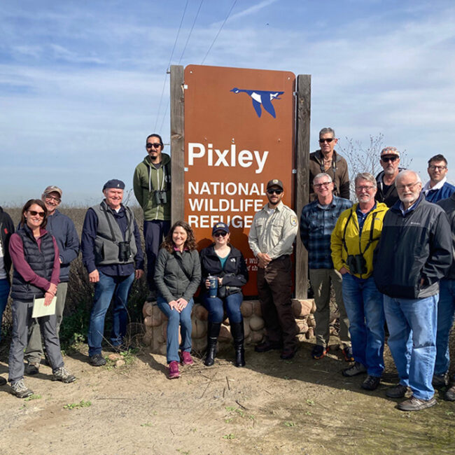 CVJV Board members and guests standing around the Pixley Wildlife Refuge sign.
