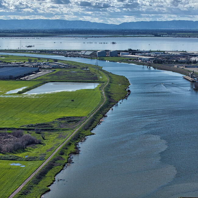 An aerial shot of a large river with flooded green fields and wetlands on each side.